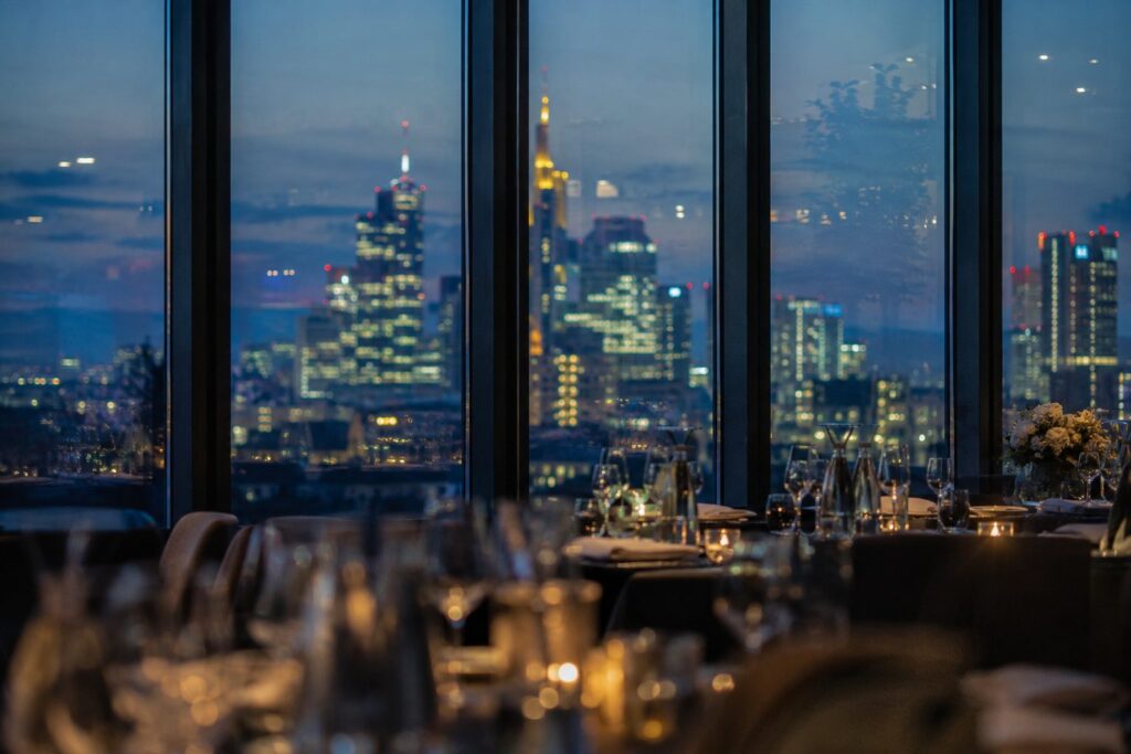 Gedeckte Tische in einer Eventlocation mit Blick auf die Frankfurter Skyline am Abend