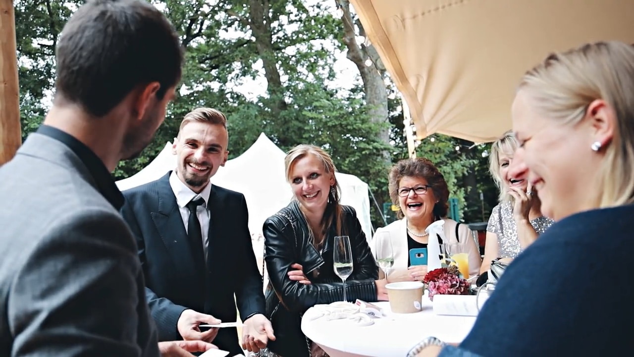 Hochzeitszauberer Oliver Henke zeigt Close-up-Magie an einem Stehtisch, die Gäste lachen